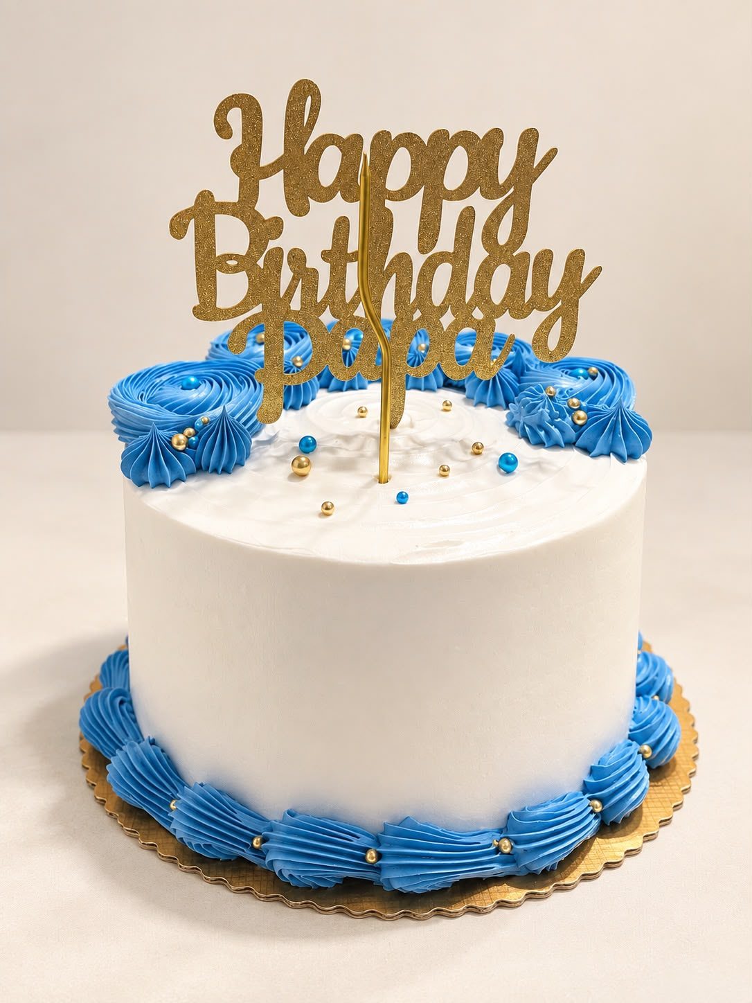 White birthday cake with blue rosettes and gold topper